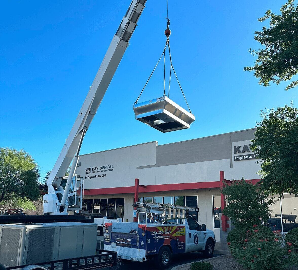 Crane lifting HVAC unit onto building roof.