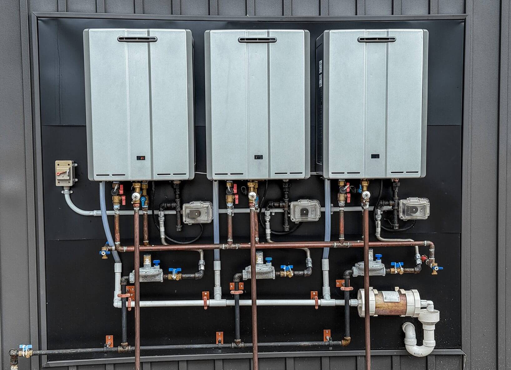 Three mounted water heaters with connected pipes.