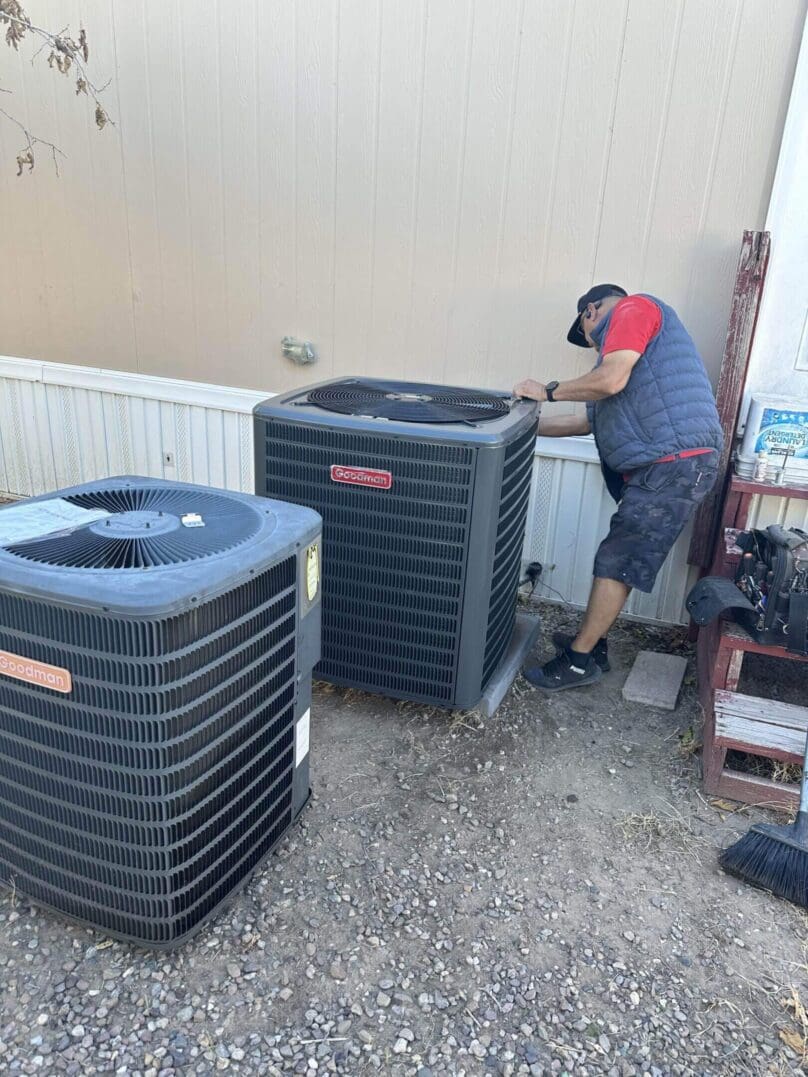 Technician working on an outdoor HVAC unit beside another unit.