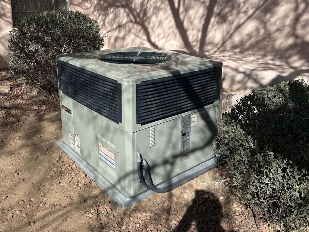 Outdoor air conditioning unit surrounded by bushes.